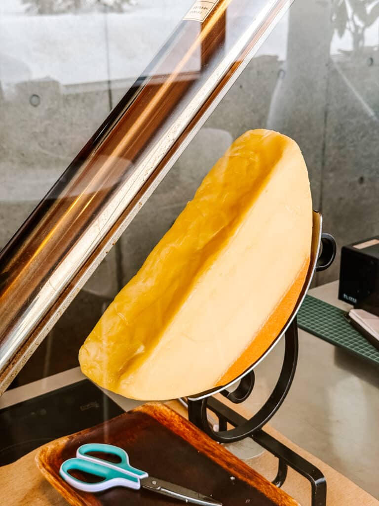 Close-up of a half cheese wheel under a heat lamp to make raclette at La Laiterie Ferme Biei
