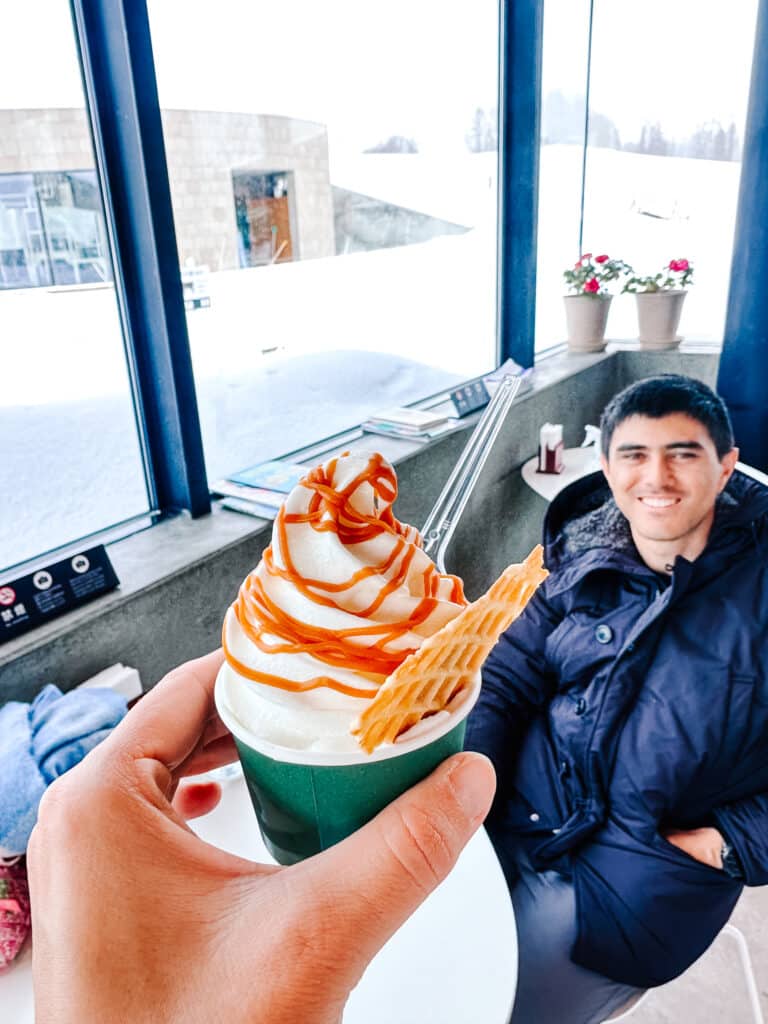 Hand holding a soft serve ice cream cone with caramel drizzle at La Laiterie Ferme Biei