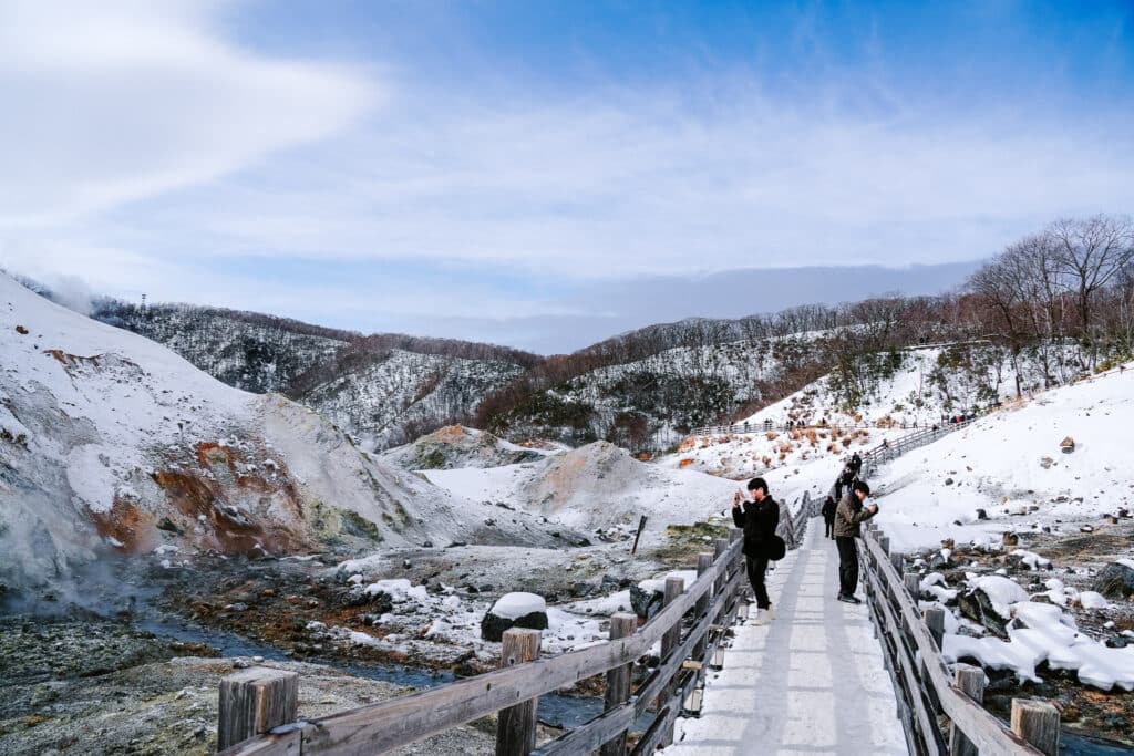 Snowy view of Noboribetsu Jigokudani Hell Valley with boardwalk trail and steaming volcanic landscape in Hokkaido, Japan.