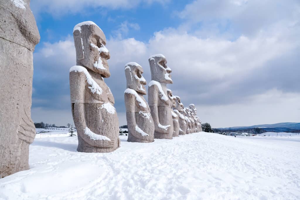 Row of large Moai statues standing in snow at Makomanai Takino Cemetery outside Sapporo, Hokkaido