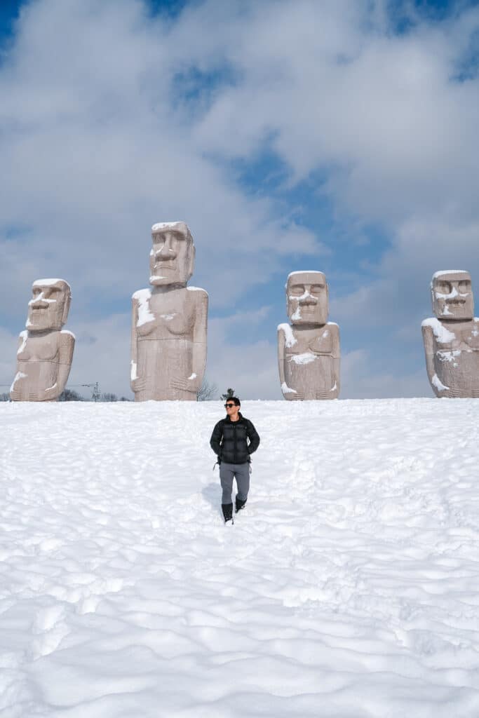 Pacific Islander visitor standing beside giant Moai statues at Makomanai Takino Cemetery in Sapporo, Hokkaido during winter