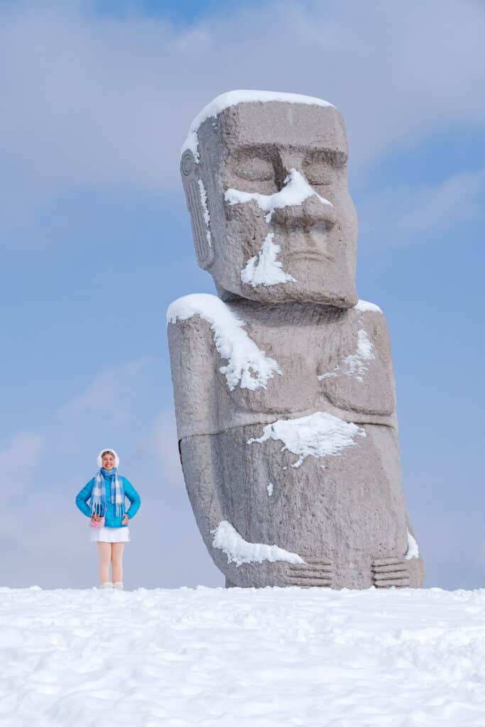 Visitor posing like a Moai statue in the snow at Makomanai Takino Cemetery in Sapporo, Japan