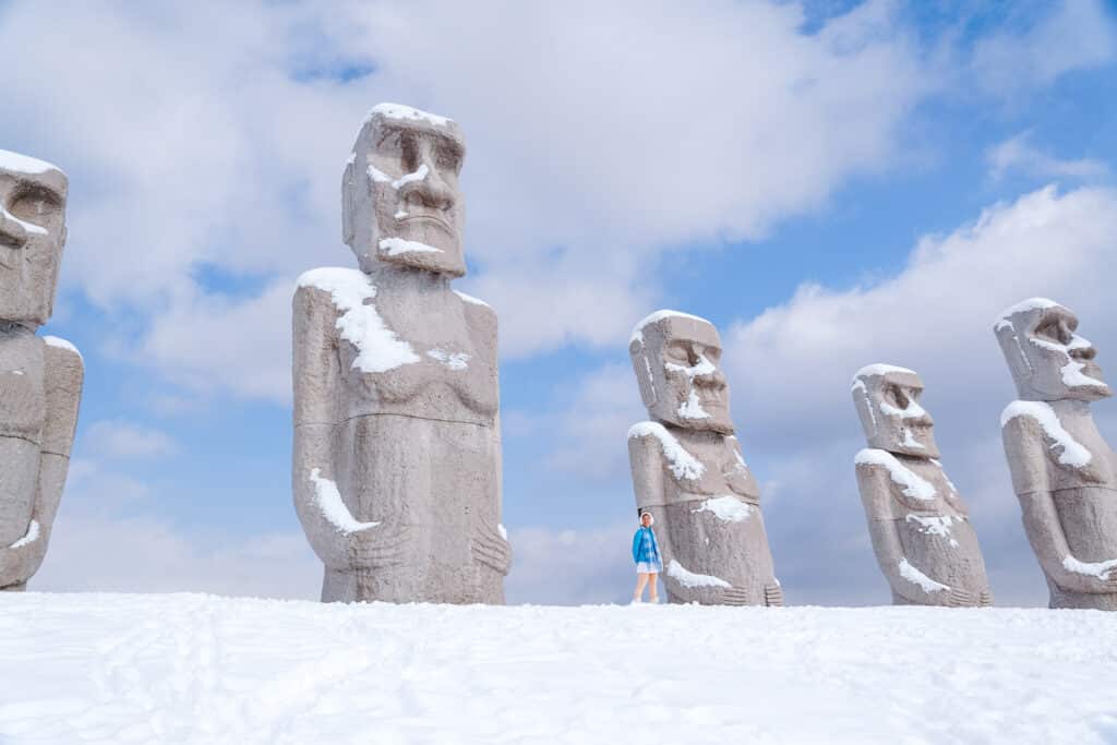 Tourist walking along the snowy Moai statue installation at Makomanai Takino Cemetery in Sapporo