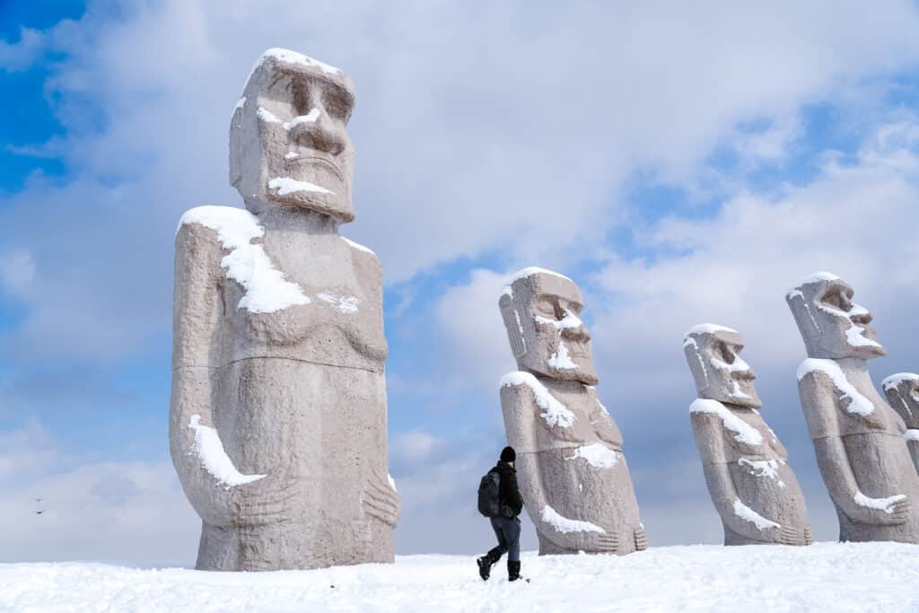 Visitor walking past a row of Moai statues in the snow at Makomanai Takino Cemetery near Sapporo, Japan