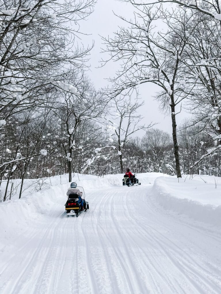 Snowmobiles riding along a groomed forest trail in deep powder near Lake Toya