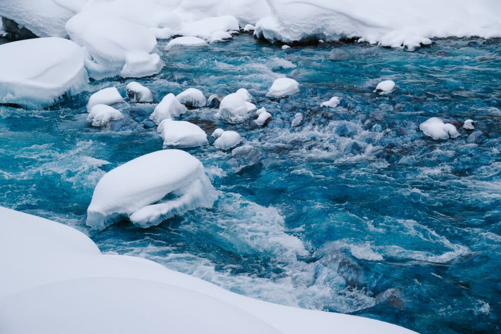 Bright turquoise water of the Shirogane Blue River flowing between snow-covered banks in winter