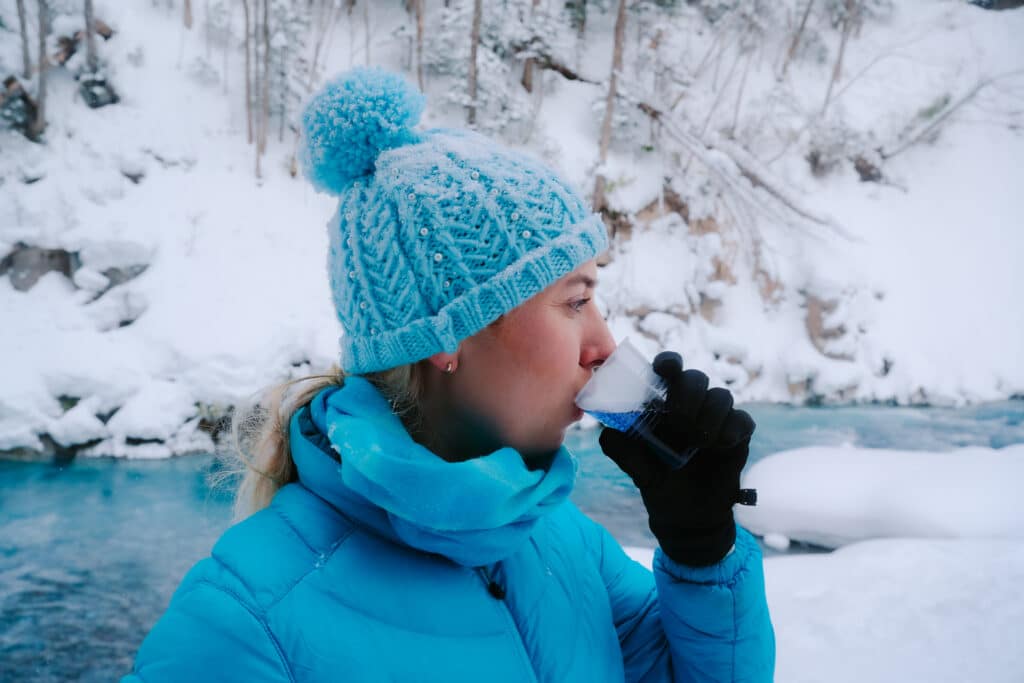 A traveler sipping a bright blue cup of buttfly pea tea in front of a bright blue river in Biei