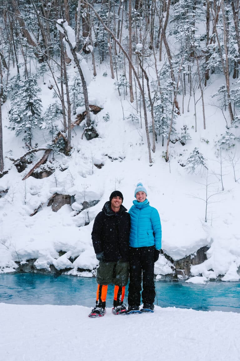Couple standing beside the Shirogane Blue River during a snowshoeing tour in Biei, Hokkaido