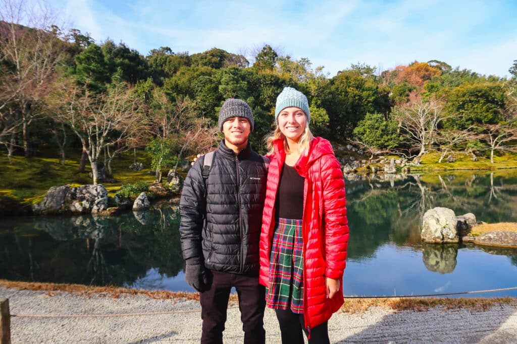 Two travelers posing in front of the koi pond in the zen garden at Tenryu-ji temple in late autumn.
