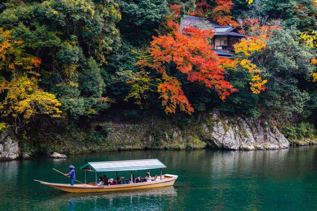 A boat floating down the river at Arashiyama, with bright autumn foliage in the river gorge.