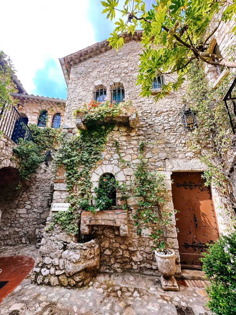 A courtyard in Eze with a fountain and trailing vines climbing the facade of a building