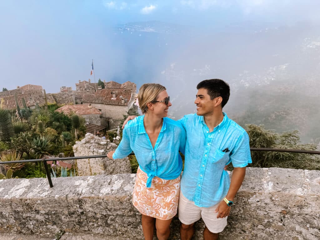 Two visitors posing at a viewpoint in the Jardin Exotique d'Eze with the Mediterranean Sea stretching out behind them