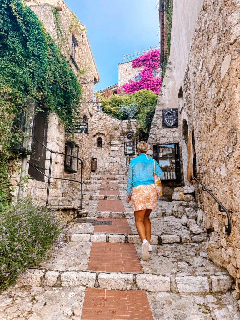 Narrow cobblestone alleyway in the medieval hilltop village of Eze on the Côte d'Azur, lined with stone walls and flowering plants