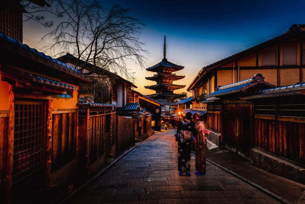 Two women in kimonos walking down the cobbled streets of the Gion district at twilight in Kyoto