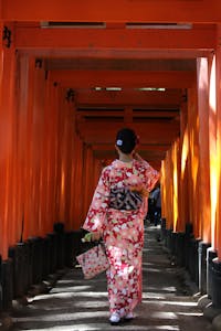 Woman wearing kimono walks through red torii gates at Fushimi Inari Shrine, Kyoto.