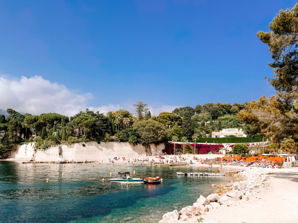 Plage Passable beach on Cap Ferrat with turquoise water, beach club area with orange umbrellas and sun loungers, and white pebbled sand