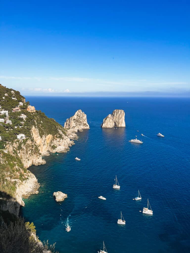 A bird's eye view over the rocky coastline of Capri with the Faraglioni rocks in the background