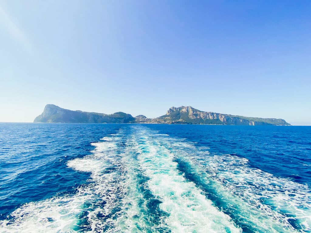 White foamy boat wake trailing across vivid turquoise Mediterranean water as Capri's rocky cliffs recede in the distance