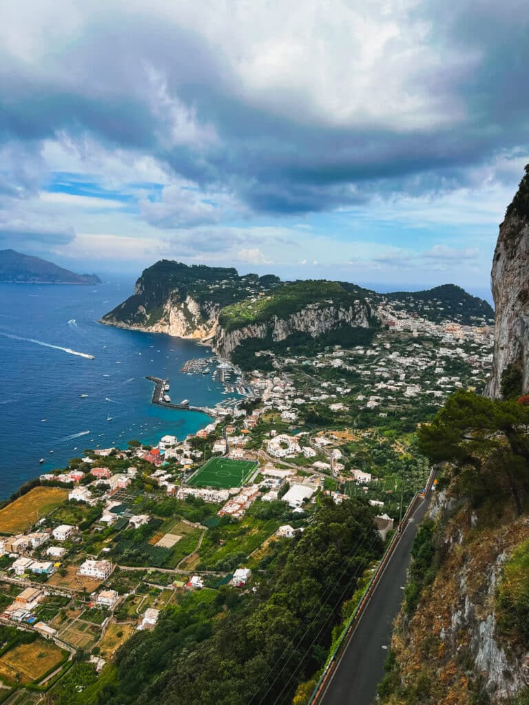 Dramatic panoramic aerial view of Capri's Marina Grande harbour and coastline with moody storm clouds rolling in, taken from a viewpoint in Anacapri