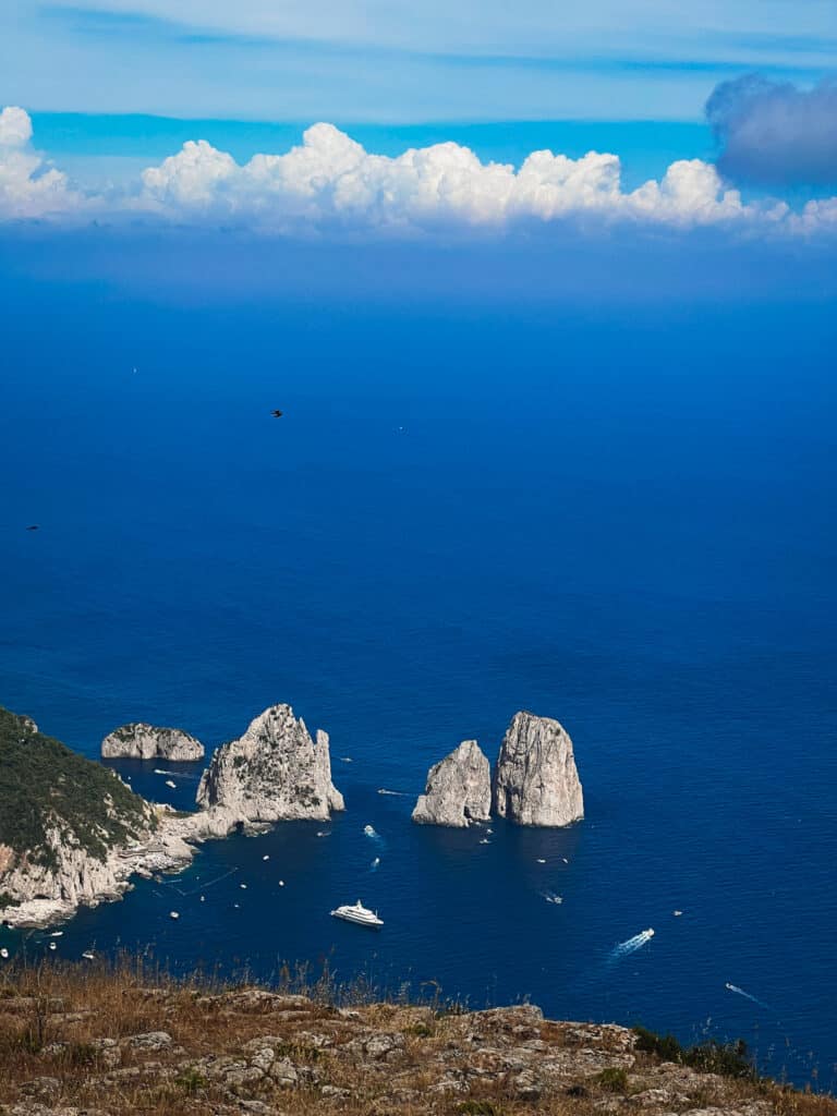 Faraglioni rocks of Capri under dramatic cumulus clouds with boats dotting the deep blue Mediterranean Sea