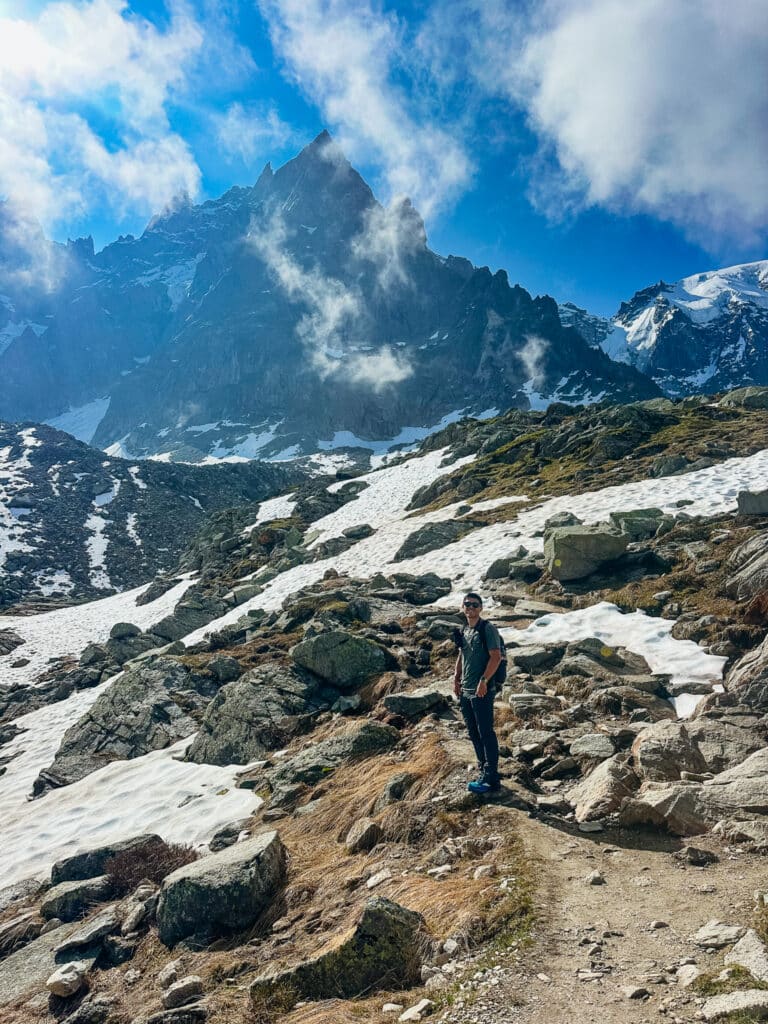 Hiker on the Grand Balcon Nord trail in Chamonix with the Aiguille du Midi rising behind patches of early-season snow