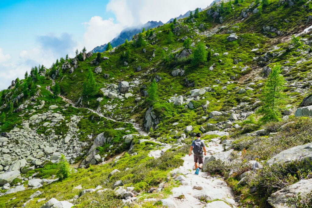 Hiker ascending a rocky green meadow on the steep approach on the Grand Balcon Nord