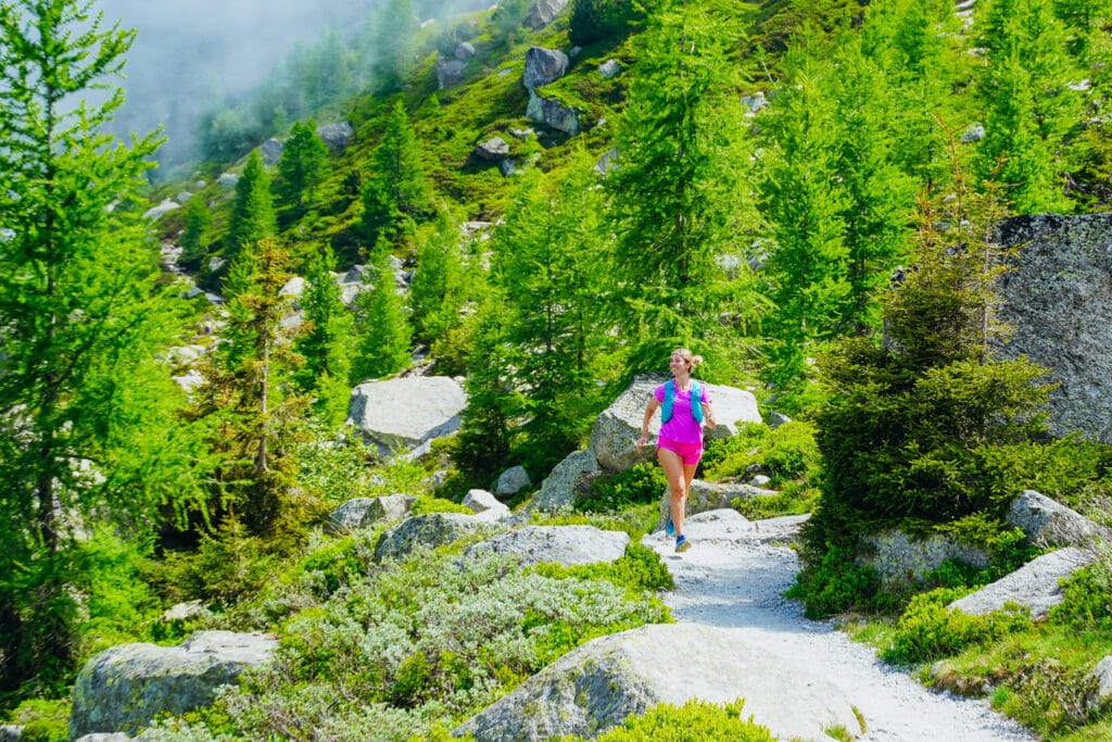 Trail runner in pink jogging through a vibrant larch forest section of the Grand Balcon Nord above Chamonix