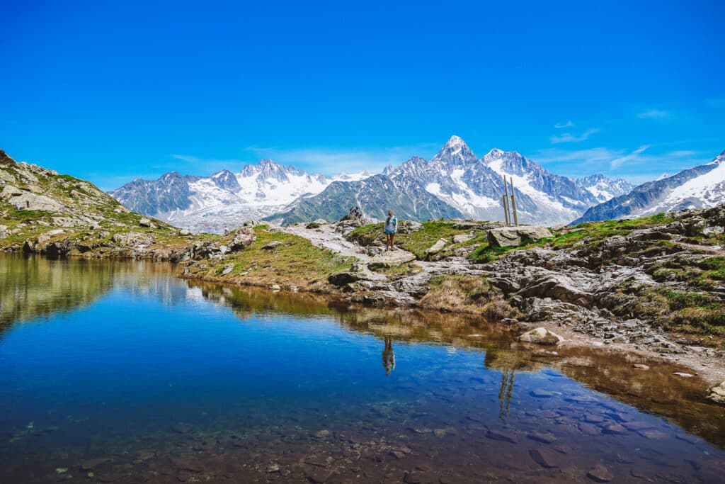 Lac des Cheserys reflecting the Aiguilles peaks in still water with a hiker pausing on the shore, Chamonix