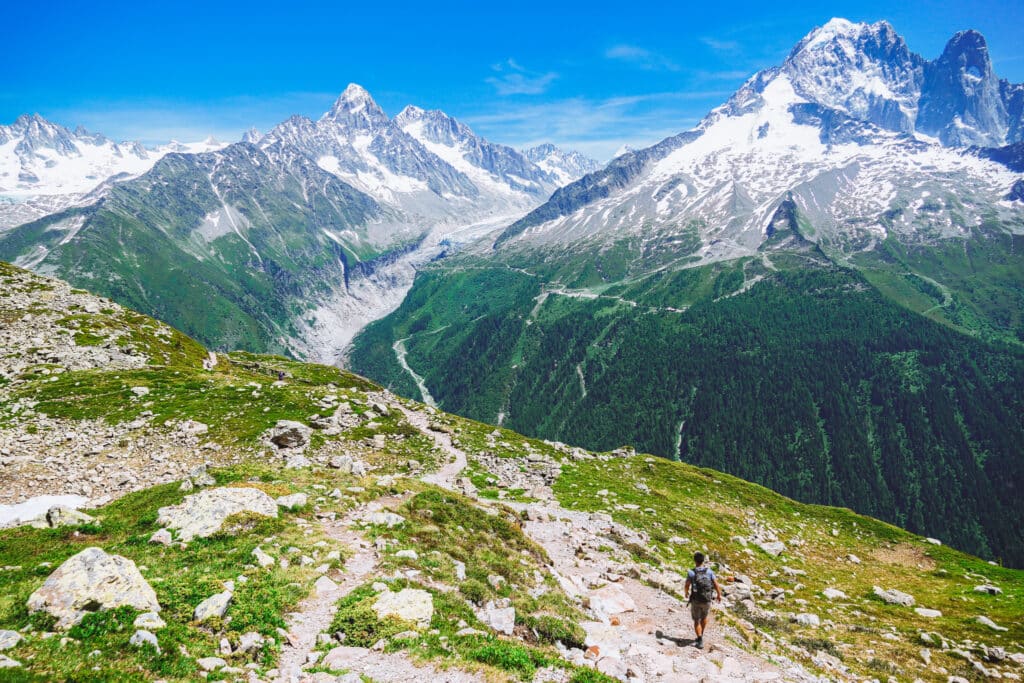 Solo hiker walking the rocky balcony trail toward Lac Blanc with the Aiguilles and Argentière glacier ahead, Chamonix