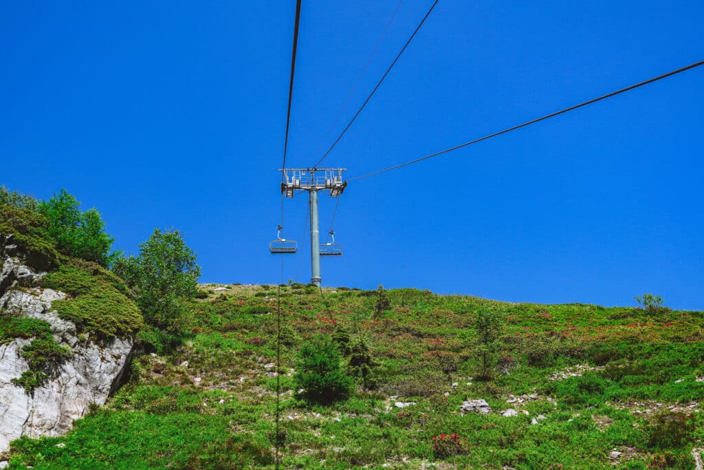 Empty L'Index chairlift cables stretching up a green hillside above the Lac Blanc trail in summer
