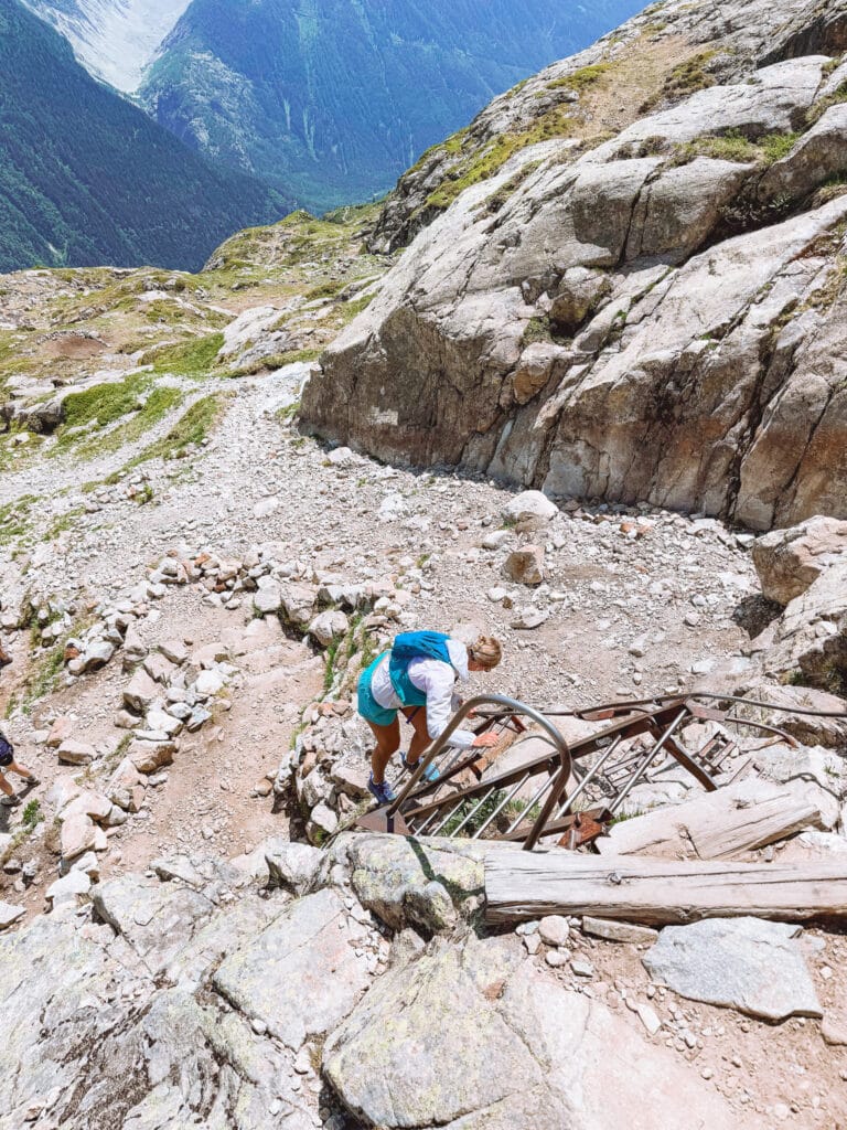 Hiker climbing a metal ladder over rocky terrain on a steep section of the Lac Blanc trail above Chamonix