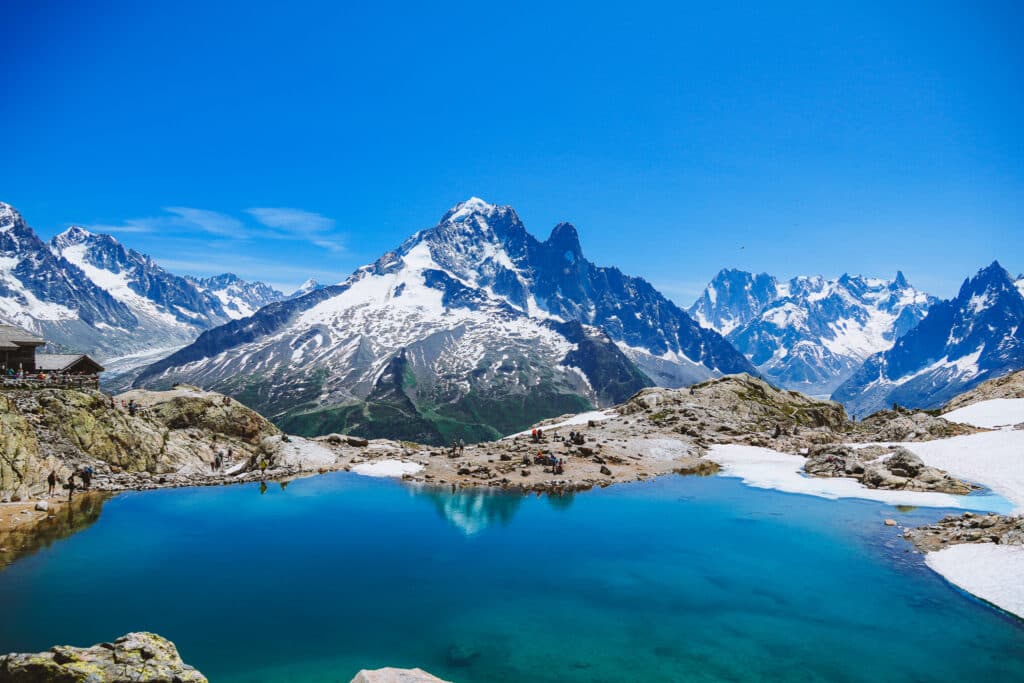 Wide view of Lac Blanc with the refuge and snow patches lining the shore beneath the Mont Blanc massif, Chamonix