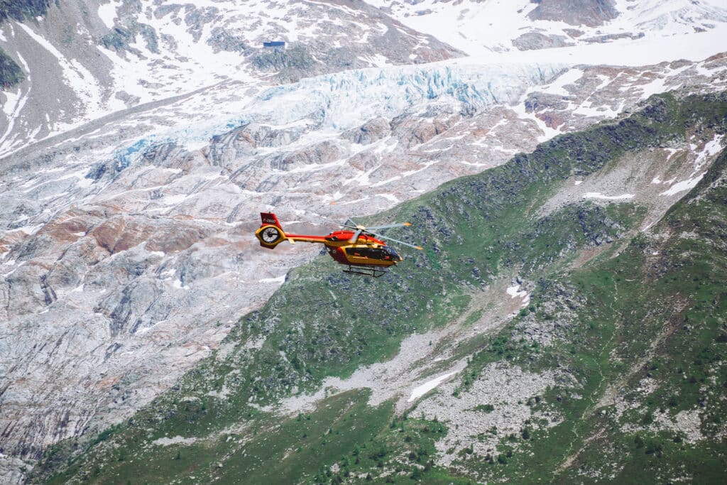 Yellow and red mountain rescue helicopter flying past the Argentière glacier high above the Lac Blanc trail