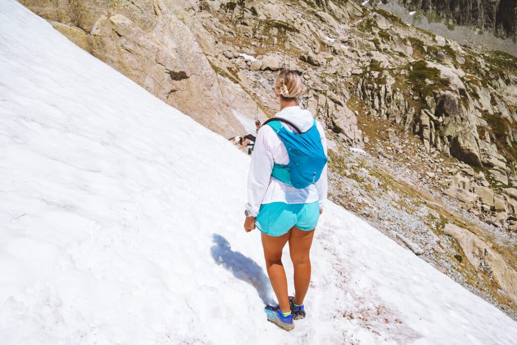 Female hiker in a turquoise running vest crossing a steep snowfield on the Lac Blanc trail in early summer near Chamonix