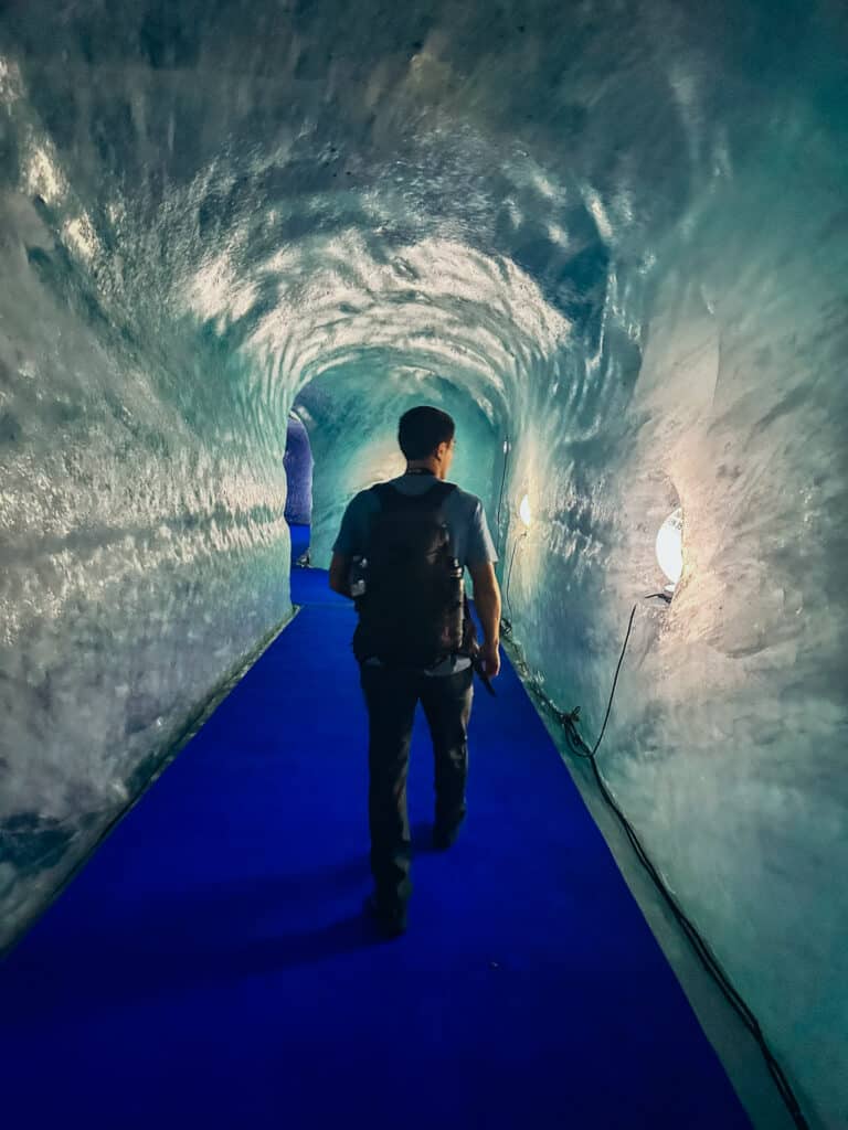 Hiker walking down the blue-carpeted entrance tunnel inside the Mer de Glace ice cave in Chamonix