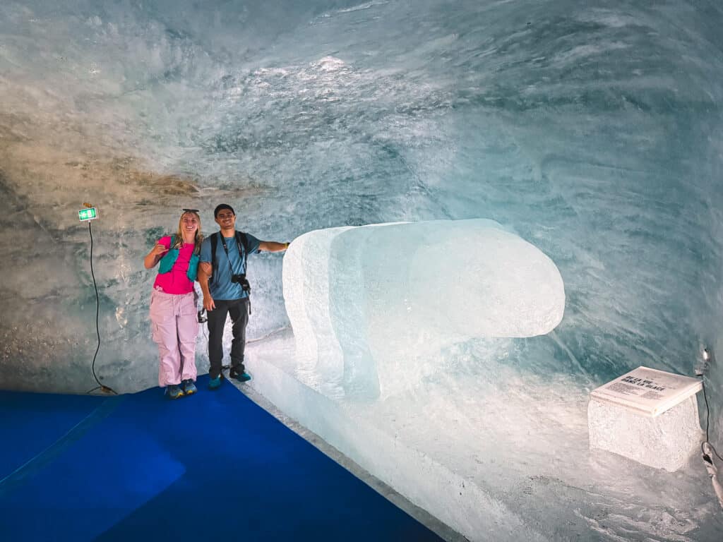 Couple posing beside a giant translucent tardigrade ice block sculpture inside the Mer de Glace ice cave