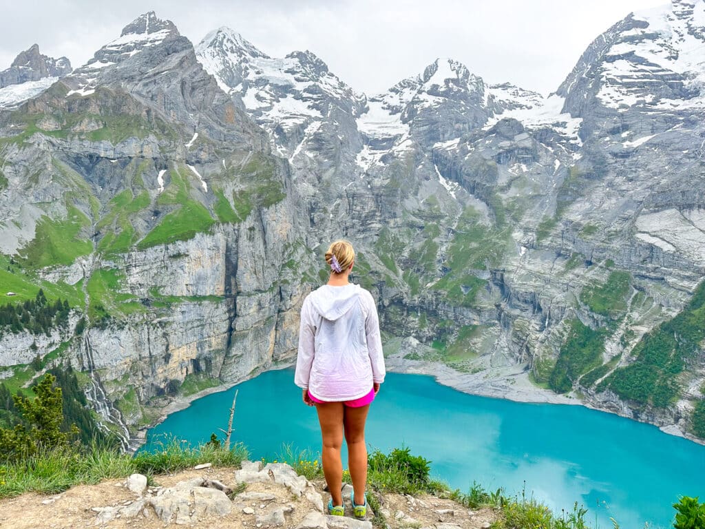 Woman standing on a rocky outcrop above Oeschinensee with a wide vista of the lake and Bernese Oberland mountains in Switzerland
