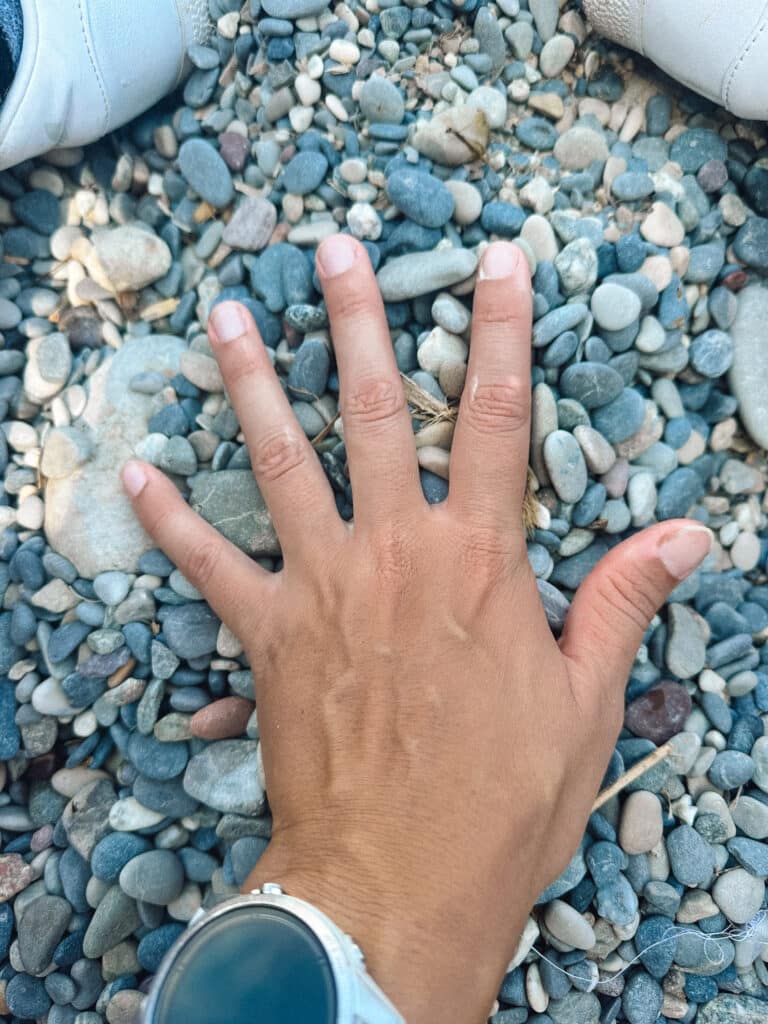 Close-up of the smooth pebbles on the beach at Paloma Beach with a hand for scale