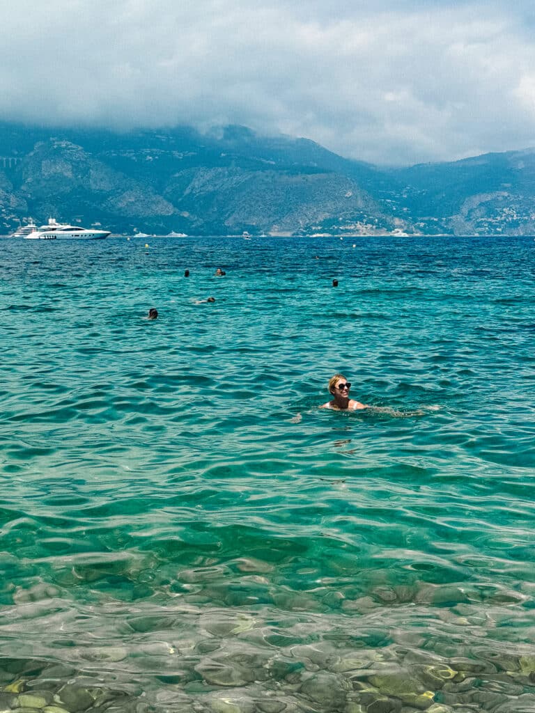 Swimmers in bright turquoise water off the coast of Paloma Beach with a yacht floating offshore in the background