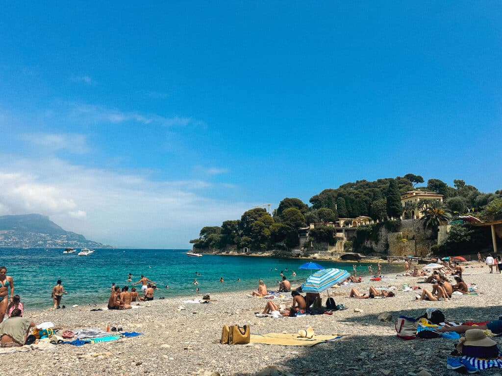 Pebble beach at Plage de la Scaletta with sunbathers and calm turquoise sea in Cap Ferrat