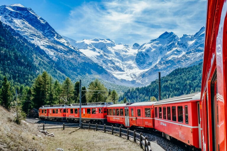 A bright red train winding between mountain peaks in Switzerland