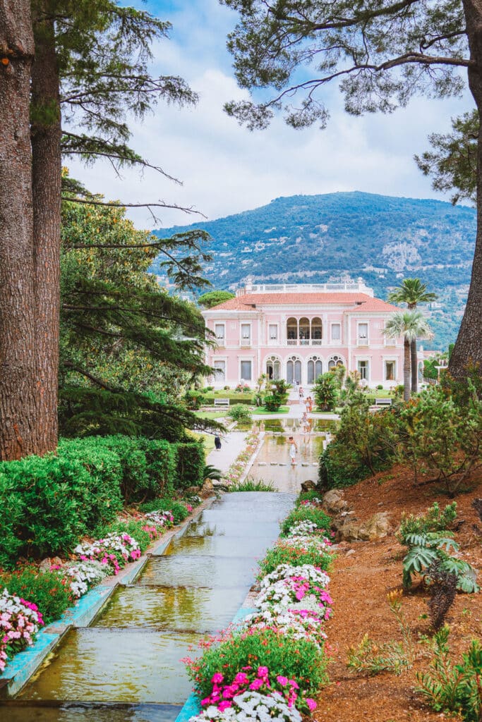 A tiered stream cascades downhill toward the pink facade of the Villa Ephrussi de Rothschild on Saint-Jean-Cap-Ferrat, South of France