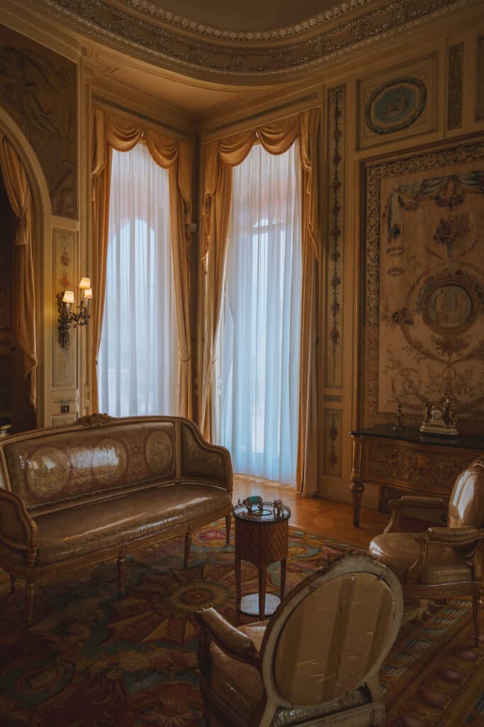Ornate interior room at Villa Ephrussi de Rothschild with antique furniture, gold detailing, and tall draped windows