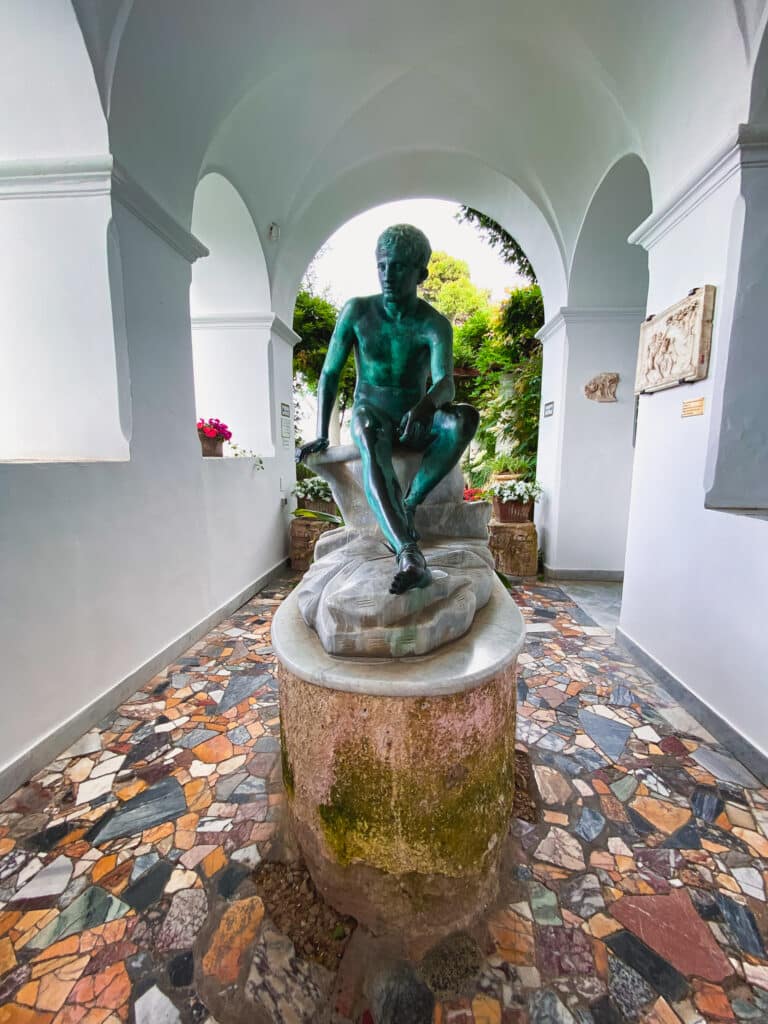 Green bronze statue in the arched white corridor of Villa San Michele in Anacapri with mosaic stone floor
