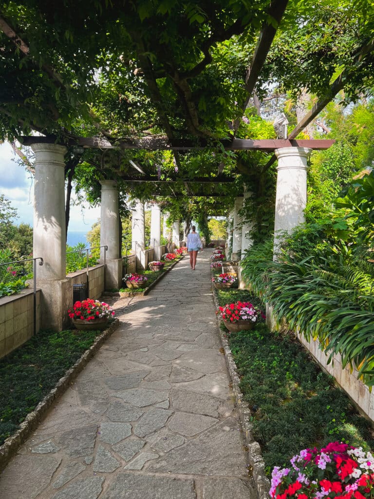 Visitor walking through Villa San Michele's sun-dappled pergola garden path lined with white columns and red flowers