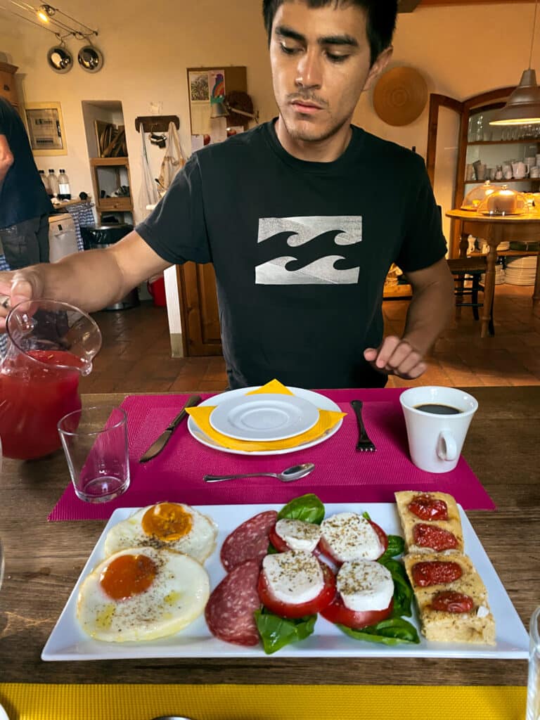 Homemade Tuscan breakfast at Agriturismo Marciano with fried eggs, salami, caprese, and tomato bruschetta beside fresh juice and espresso.
