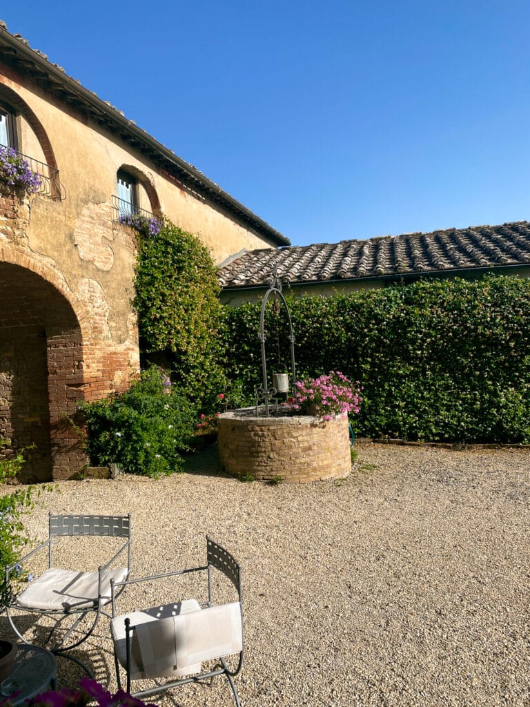 Stone well, climbing greenery, and the warm ochre facade of the main guesthouse courtyard at Agriturismo Marciano outside Siena.