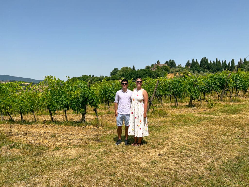 Couple in summer clothes posing among the grapevines with a hilltop Tuscan village in the background at Agriturismo Marciano.