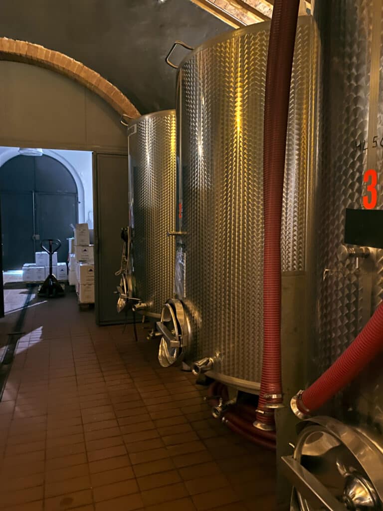 Stainless steel fermentation tanks lining the brick-arched wine cellar at La Lastra in Siena