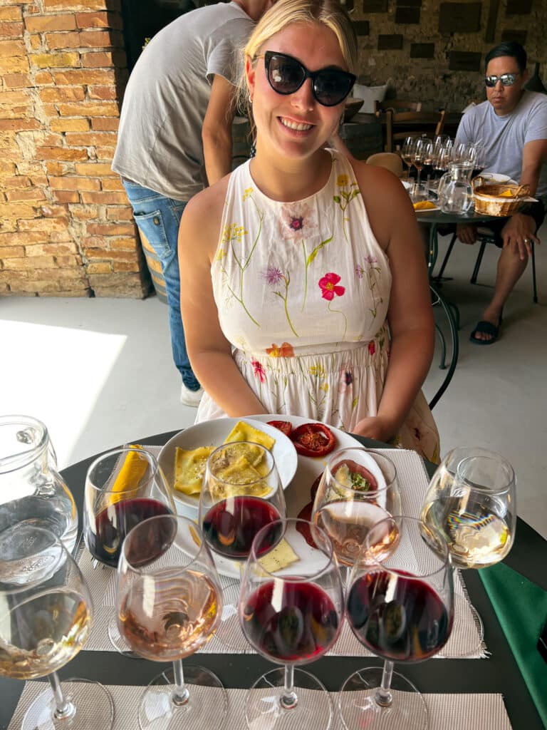 Woman holding a wooden tray with a flight of red and white wines and small antipasti plates at Agriturismo Marciano.